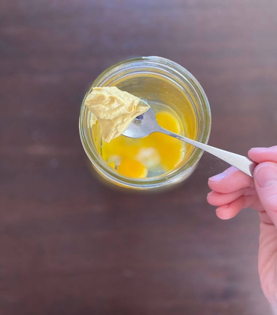 Adding dijon mustard to a jar of raw eggs.