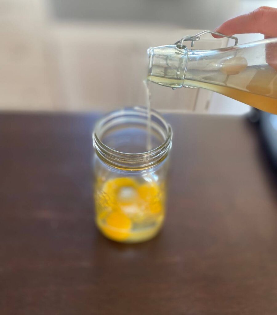 Pouring apple cider vinegar into a jar of raw eggs.