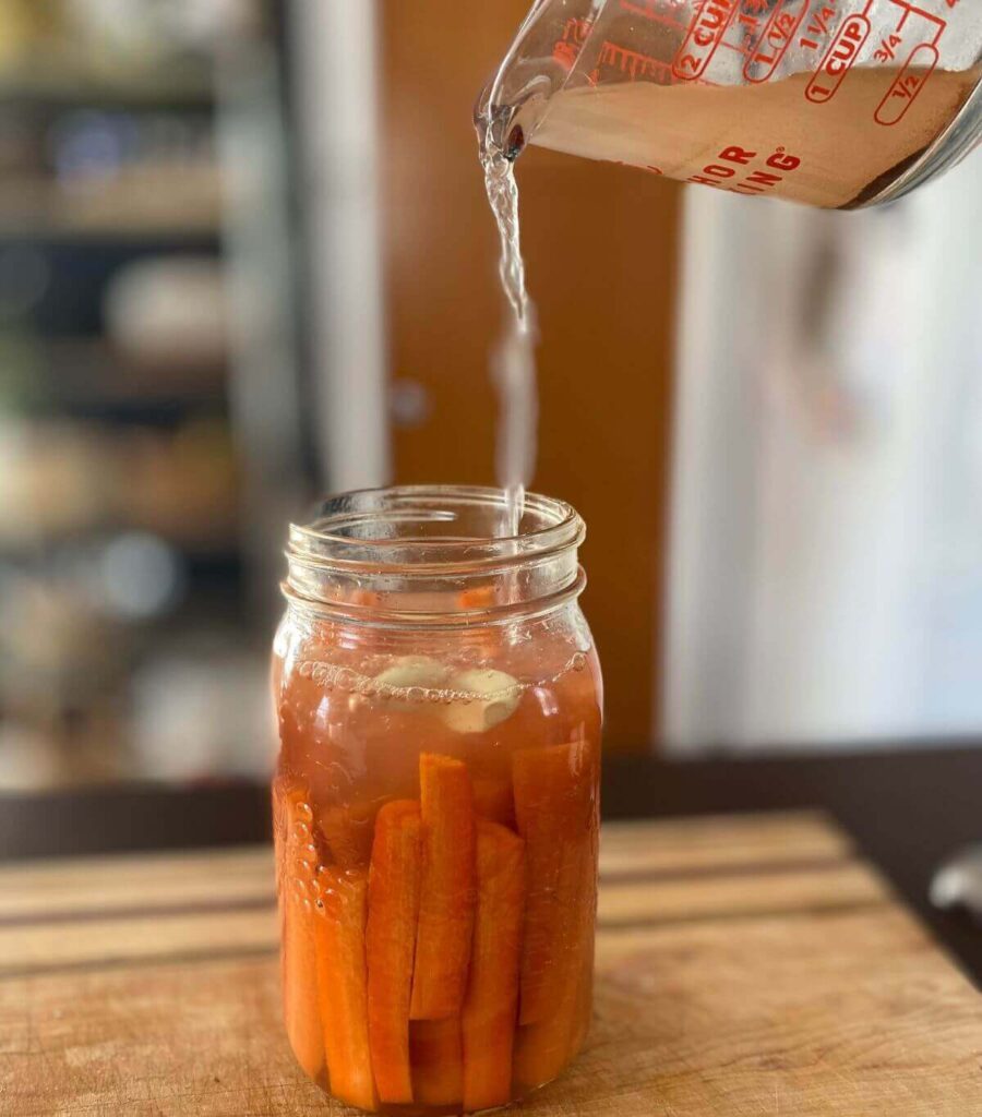 pouring salt water over carrots and garlic in a jar ready to ferment