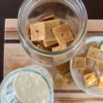 A jar of sourdough crackers, sourdough discard and crackers and cheese in the background.