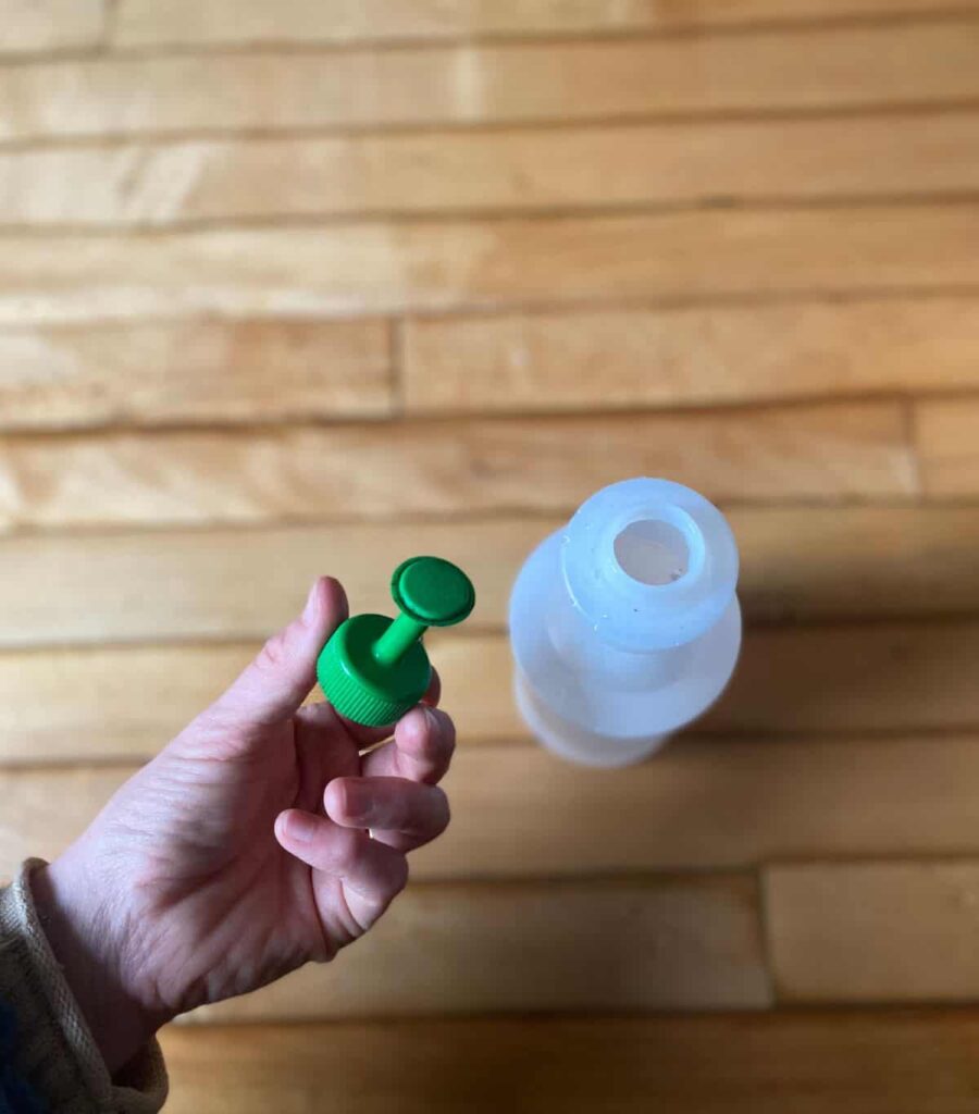 Holding a sprayer nozzle above a water bottle