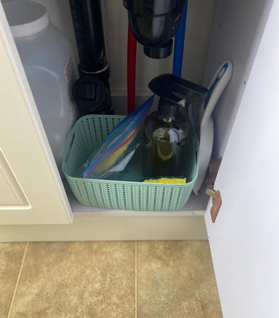 A blue plastic basket in a bathroom cupboard, stocked with bathroom cleaning supplies.