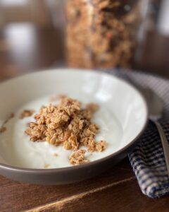 Close up shot of a bowl of yogurt and homemade granola with a jar full blurred in the background.