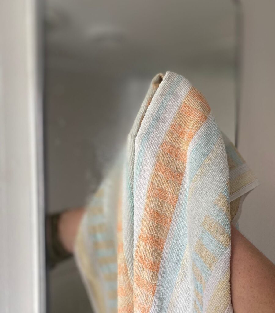Wiping down a sprayed bathroom mirror with a colourful hand towel.