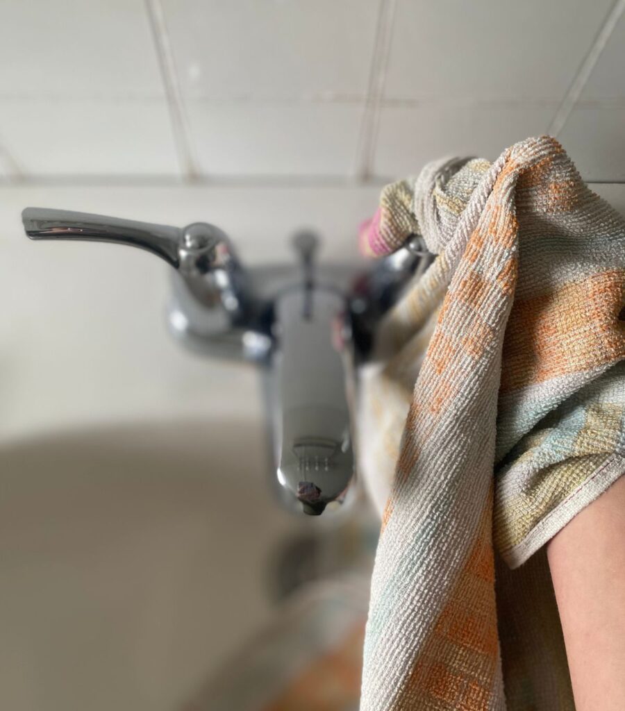Wiping down chrome bathroom faucet with a colourful hand towel.
