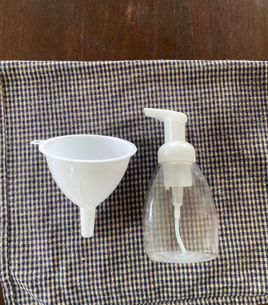 An empty hand soap dispenser and a bottle funnel laying on a tea towel.