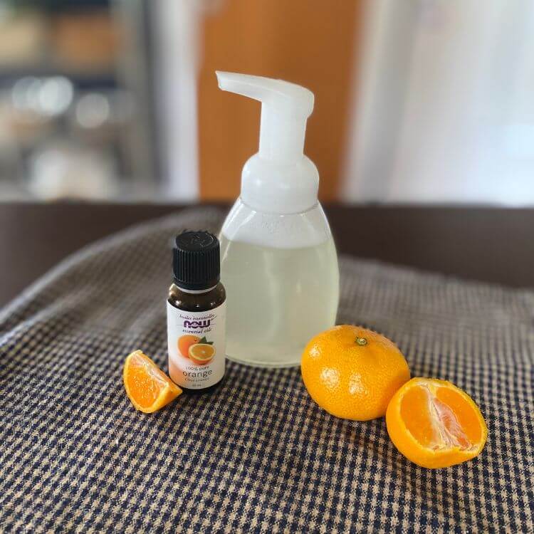 A soap dispenser of homemade hand soap without Castile, orange essential oil and clementines cut in have an sliced on a tea towel.