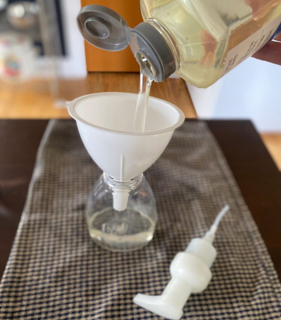 Pouring liquid soap through a bottle funnel into a soap dispenser.