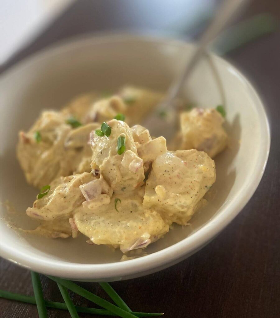 Close up shot of loaded potato salad in a white bowl topped with fresh chives.