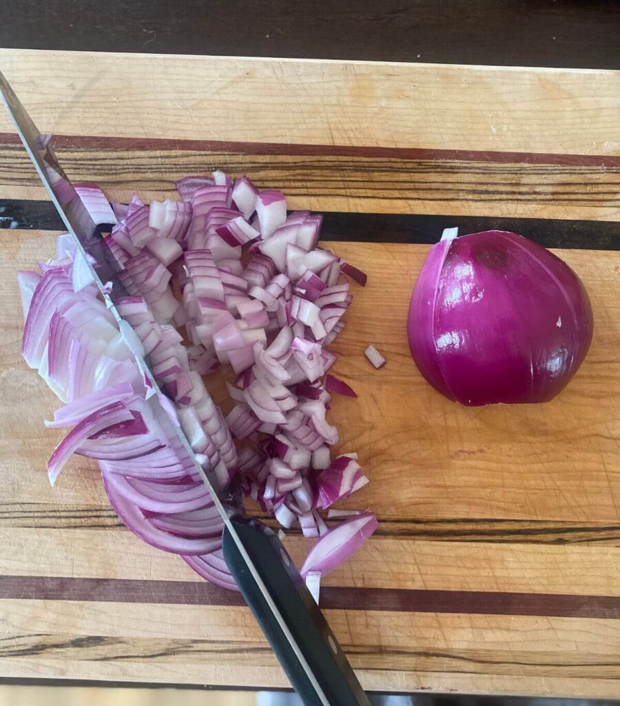 Chopping a bright red onion on a decorative wooden cutting board with a large knife.