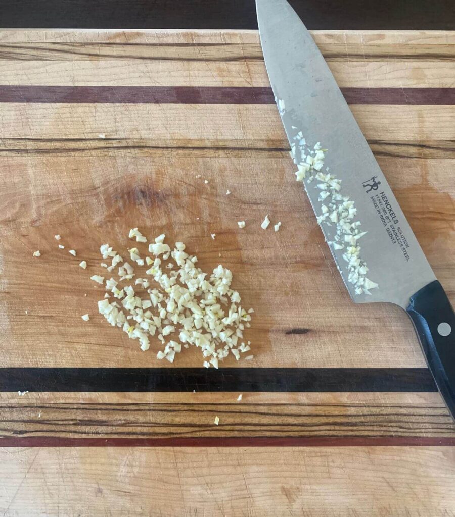 Mincing fresh garlic on a wooden cutting board.