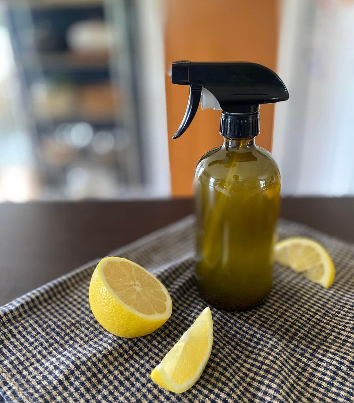 the-humming-homemaker-homemade-bathroom-cleaner-featured-image A glass spray bottle of homemade bathroom/household cleaner with sliced lemons displayed on a table.